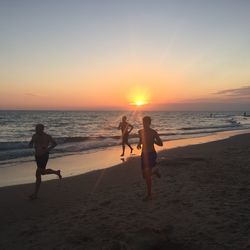 Shirtless men running at beach against sky during sunset