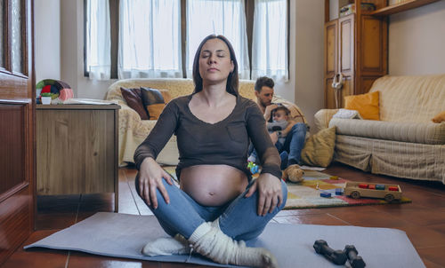 Mother exercising while father playing with son in background at home