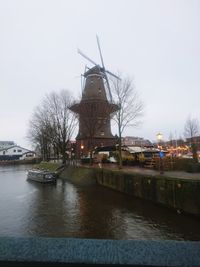 Traditional windmill by river against sky