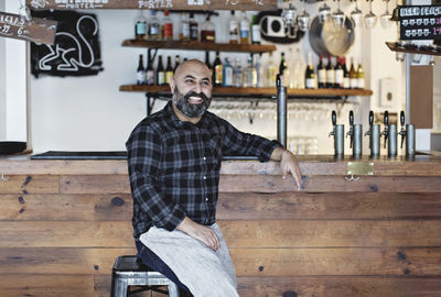 Confident smiling bartender sitting by bar counter