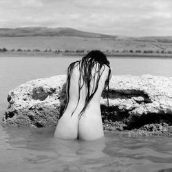 Rear view of woman on rock at beach against sky