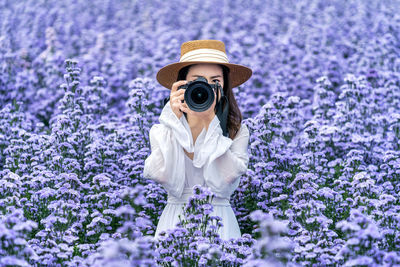 Portrait of woman photographing while standing in flowering field