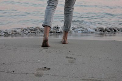 Low section of man walking on shore at beach