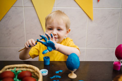 Little boy draws blue paint on his hand, paints an easter egg