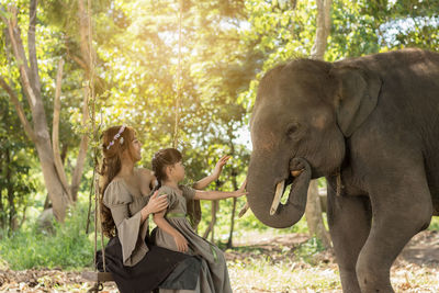 Woman with daughter touching elephant in forest