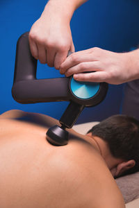 Medium shot of caucasian professional male massage therapist getting back muscles with massage gun