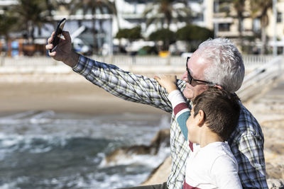 Man with grandson taking selfie at beach