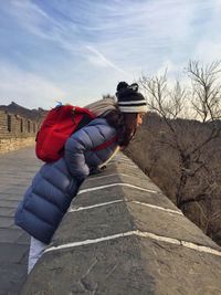 Side view of woman leaning on fortified wall against sky