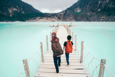 Rear view of mother with son walking on pier over lake