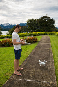 Side view of young man holding drone remote drone on walkway at park