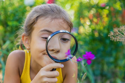 Cute girl looking at flower through magnifying glass