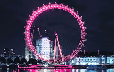 Illuminated ferris wheel by river at night