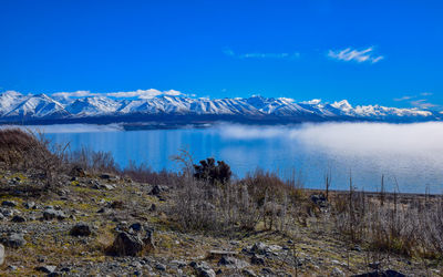 Scenic view of lake and snowcapped mountains against blue sky