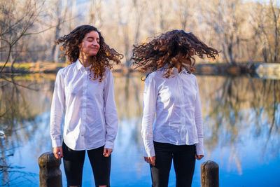 Sisters with tousled hair standing by lake
