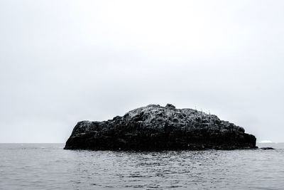 Rock formation in sea against clear sky