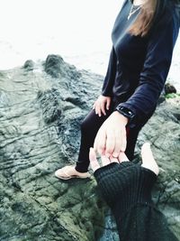 Low section of woman sitting on rock by sea