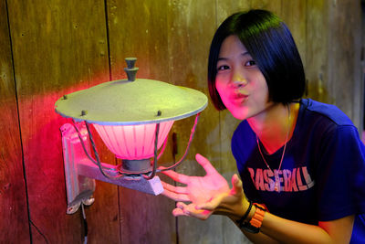 Portrait of young woman standing by lighting equipment on wooden wall