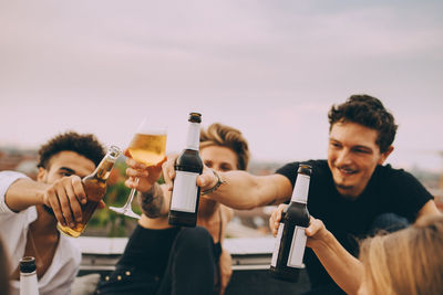 Friends celebrating with beer while enjoying in rooftop party at city