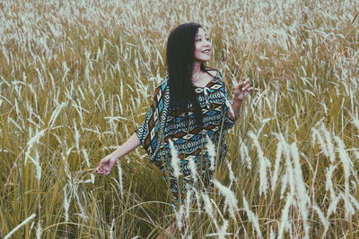 Young woman looking away while standing amidst plants on field