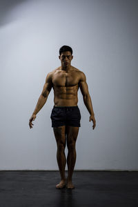 Portrait of shirtless muscular man exercising against wall