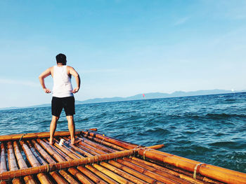 Rear view of man standing on pier over sea against sky