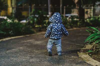 Rear view of girl wearing hooded shirt while walking on road