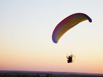Low angle view of man flying powered parachute against clear sky during sunset