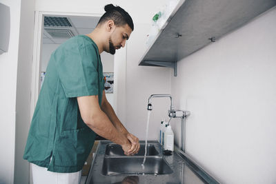 Side view of male nurse washing hands in sink at hospital