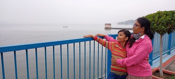 Mother and son embracing while standing by railing against sea