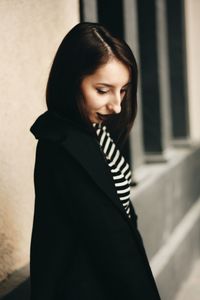 Young woman wearing black coat standing against wall