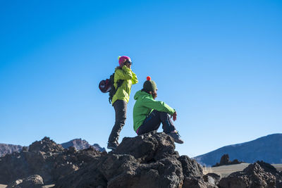 Low angle view of hikers on rocks against clear blue sky