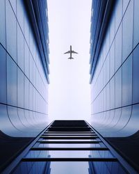 Low angle view of modern building against airplane flying in clear sky