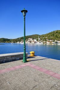 Street light by lake against clear blue sky