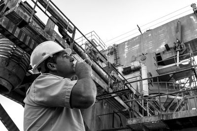 Low angle view of construction worker smoking cigarette while looking at factory