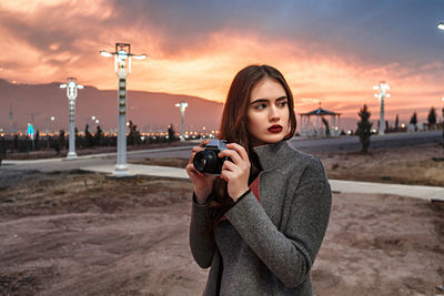 Portrait of young woman photographing at sunset