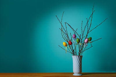 Front view of a white vase with a branch decorated with eggs on blue background. easter in germany.