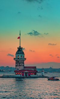 Lighthouse by sea against sky during sunset