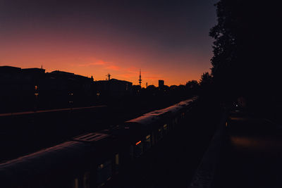 Silhouette buildings and train in city against sky during sunset