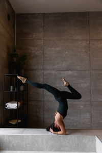 Young sporty attractive woman practicing yoga doing headstand exercise