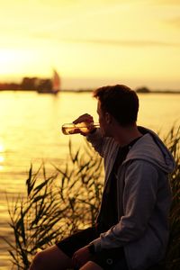 Teenage boy drinking by lake during sunset