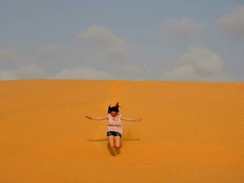 Woman jumping at desert against sky