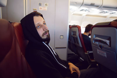 Man in a black jacket with a hood is a passenger of the plane sitting on a chair