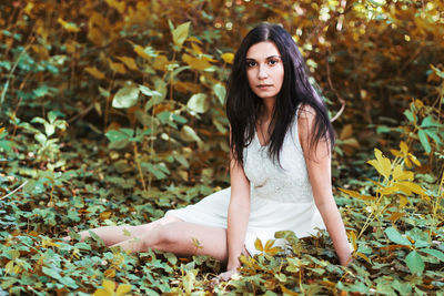 Portrait of beautiful young woman sitting in forest during autumn