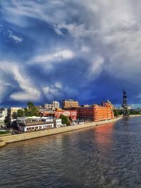 Buildings at waterfront against cloudy sky