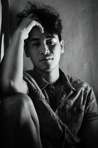 Close-up portrait of young man sitting against wall