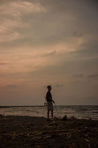 Man standing on beach against sky during sunset