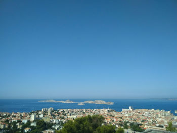 Aerial view of townscape by sea against clear blue sky