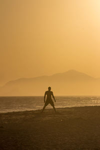 Silhouette man standing on beach against clear sky during sunset