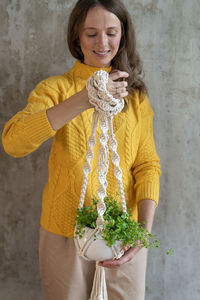 Smiling woman holding plant against wall at home