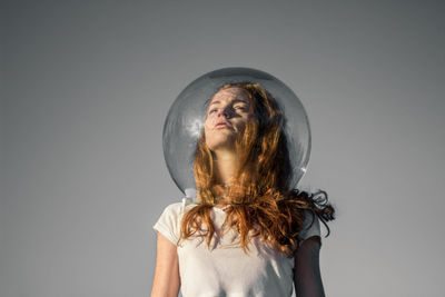 Thoughtful young woman wearing glass helmet in head against gray background